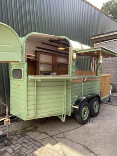 an old green trailer is parked in front of a building with a kitchen on it