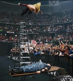 a man falling off a ladder in front of an audience at a wrestling match,