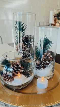 three clear glass vases with pine cones and candles on a table in a living room