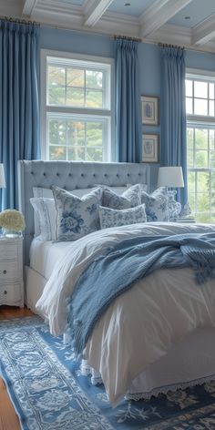 a bedroom with blue walls and white bedding, windows, and rugs on the floor