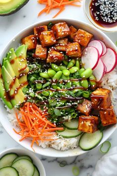 a white bowl filled with rice, vegetables and tofu on top of a table