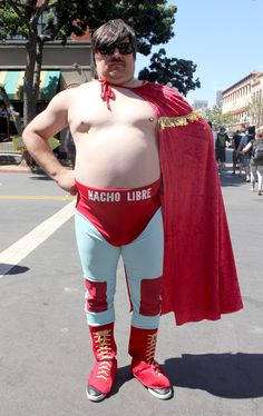 a man in a red cape and blue pants is standing on the street with his hands on his hips