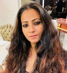 a woman with long hair sitting in front of a table and looking at the camera