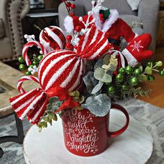 a red coffee cup filled with candy canes and greenery on top of a table