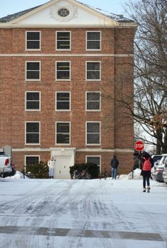 two people skating in front of a brick building on a snow covered street with stop signs