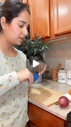 a woman standing in a kitchen preparing food on top of a wooden cutting board next to a potted plant