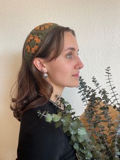 a woman wearing a headband with flowers and leaves on it, standing next to a wall