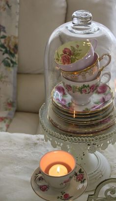 a glass clochet with tea cups under it and a lit candle on the table