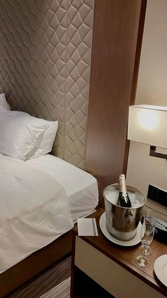 a bottle of wine sitting on top of a metal bucket next to a bed with white sheets