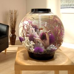 a fish bowl filled with purple and white flowers on top of a wooden coffee table