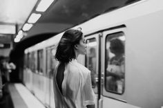 a woman is waiting for the train to arrive at the subway station in black and white