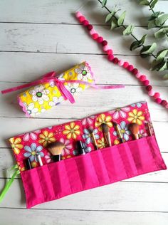 a pink bag with makeup brushes in it on a white wooden floor next to flowers