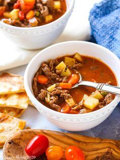 two bowls of beef and vegetable soup with pita bread on the side