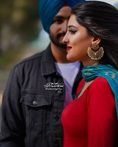 a man standing next to a woman in a red dress and blue turban