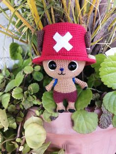 a crocheted stuffed animal wearing a red hat next to green leaves and plants