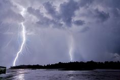 two lightning strikes in the sky over a body of water with trees on either side