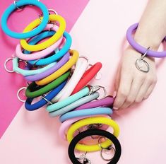 a woman's hand is holding several different colored bracelets on a pink and white background