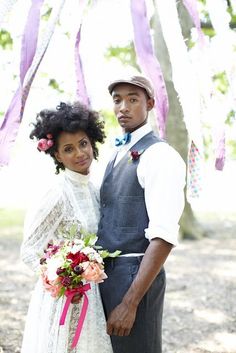 a man and woman standing next to each other in front of a tree with ribbons