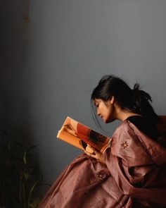 a woman sitting on a bed reading a book with her hair blowing in the wind