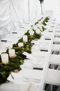 the long table is covered with moss and lit candles for an elegant touch to the reception