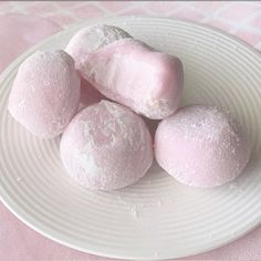 four pink marshmallows are on a white plate next to some powdered sugar