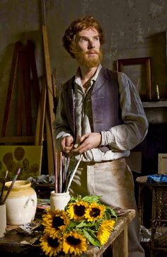 a man in an art studio with sunflowers on the table next to him