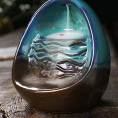 a glass candle holder sitting on top of a piece of wood with a boat in it