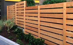 a wooden fence next to a building with plants growing on the sides and bushes in front