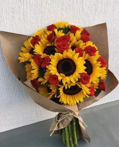 a bouquet of sunflowers and red roses wrapped in brown paper on a table