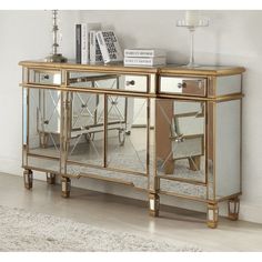 a gold mirrored cabinet with two drawers and three mirrors on the front, along with a white rug