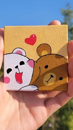 a hand holding up a small painting of two bears and a bear cub with hearts on it