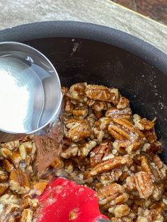 pecans are being mixed in a pot with a red spatula to stir them