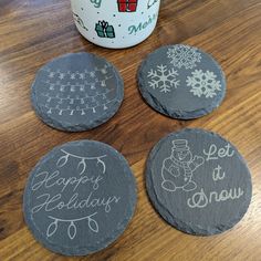 four slate coasters with handwritten words and snowflakes on them next to a coffee mug