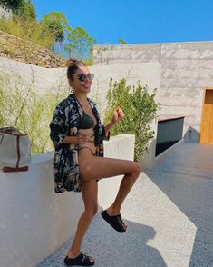 a woman in a bathing suit posing on a wall with her leg up and legs crossed