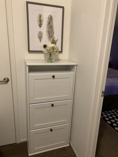 a white dresser with flowers on top in a room next to a bed and door