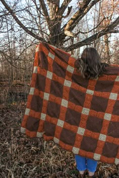 a woman is standing in the woods with a blanket over her head and there is a tree behind her