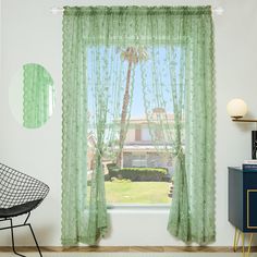 a window with green curtains and a chair in front of it, next to a plant