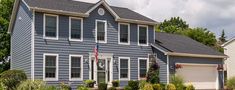 a large blue house with white trim and two story windows on the front, surrounded by landscaping