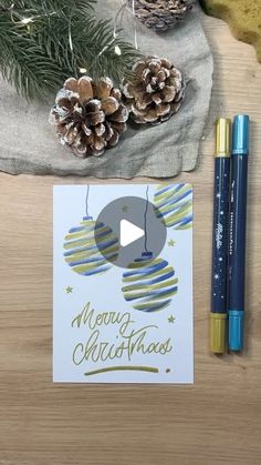 a christmas card next to two pens and some pine cones