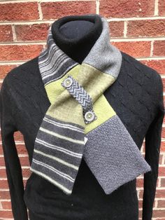 a gray and green scarf on a mannequin's dummy stand in front of a brick wall