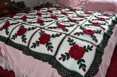 a crocheted bedspread with red flowers on it and green trim around the edges