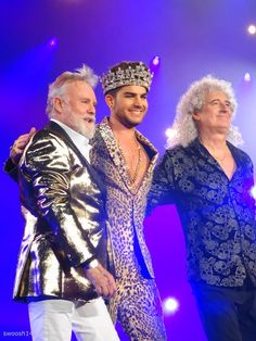 the three men are dressed in gold and blue outfits on stage with their arms around each other