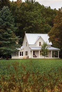 a white house sitting in the middle of a lush green field next to tall trees