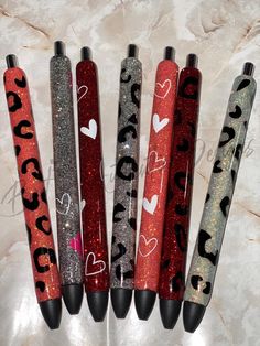 four pens are lined up in the shape of hearts and leopard print, on a marble surface