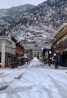 a snowy street with buildings and mountains in the background