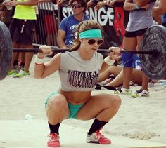 a woman squats while holding a barbell in front of her and people watching