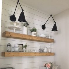 three wooden shelves with hanging lights and dishes on them in a white kitchen, against the wall