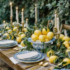 the table is set with lemons and blue china plates, gold candles, and greenery