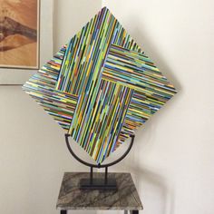 a sculpture made out of strips of colored paper on top of a marble table next to a painting