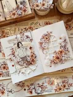 an open book with flowers on it sitting on top of a table next to other cards